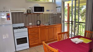 Une cuisine compacte équipée d’une cuisinière, d’un four à micro-ondes et d’un évier. On y trouve une table à manger recouverte d’une nappe rouge et une chaise.