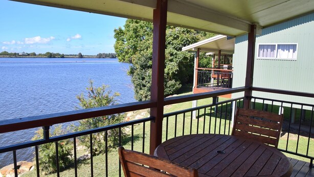 Un balcon avec une table et des chaises en bois, donnant sur un lac dont on aperçoit au loin le rivage et les arbres.