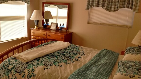 A bedroom with a bed, a dresser, a mirror, and a window with blinds.