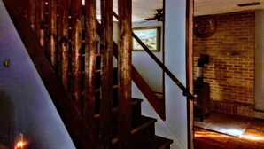 Unes escales de fusta amb barana metàl·lica que condueixen a una habitació amb paret de maó i un quadre al mur.