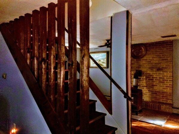 Una escalera de madera con barandilla metálica que lleva a una habitación con pared de ladrillo y un cuadro enmarcado en la pared.