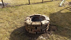 Una xemeneia rodona feta de maons apilats en una zona exterior enjardinada.