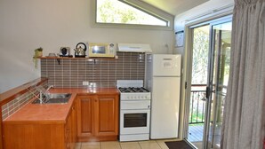 A compact kitchen with a gas stove, microwave, and refrigerator. It features wooden cabinets and a tiled backsplash. - Coast & Country Cabin 4 (Rainbow Reach)