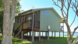 A two-story house with a balcony, wooden staircase, and a view of the water. - Coast & Country Cabin 4 (Rainbow Reach)
