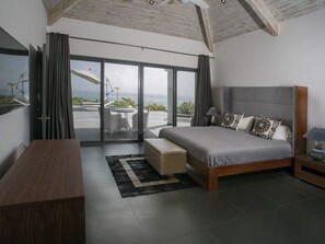 Ein modernes Schlafzimmer mit einem großen Bett, einem Schreibtisch und Blick ins Freie durch eine Schiebetür.