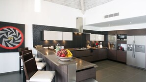 Una cocina moderna con una isla central, muebles oscuros, electrodomésticos de acero inoxidable y un cuadro abstracto rojo en la pared.