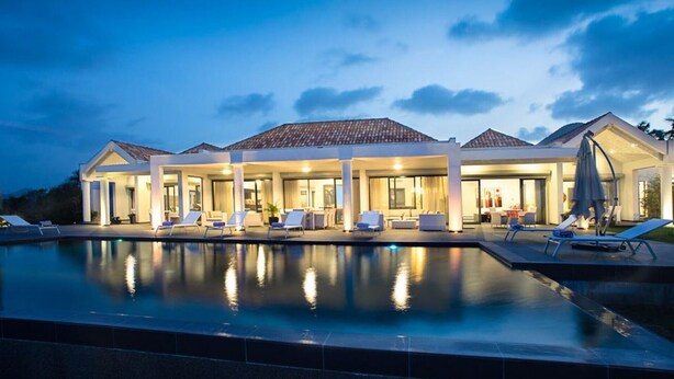 Un resort moderno con una piscina grande, mobiliario exterior y un patio cubierto.