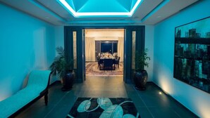 Un interior moderno con techo iluminado en azul, un comedor con mesa y sillas, y un cuadro abstracto grande en la pared.