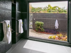 Ein modernes Badezimmer mit dunkel gefliesten Wänden, einer Duschkabine aus Glas und Blick auf einen angelegten Garten.