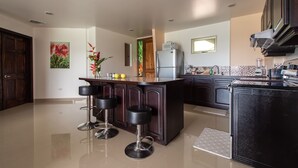 Uma cozinha moderna com uma ilha central, banquetas, geladeira e micro-ondas.