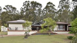 Uma casa moderna de dois andares com telhado plano, varanda coberta e um pequeno jardim.