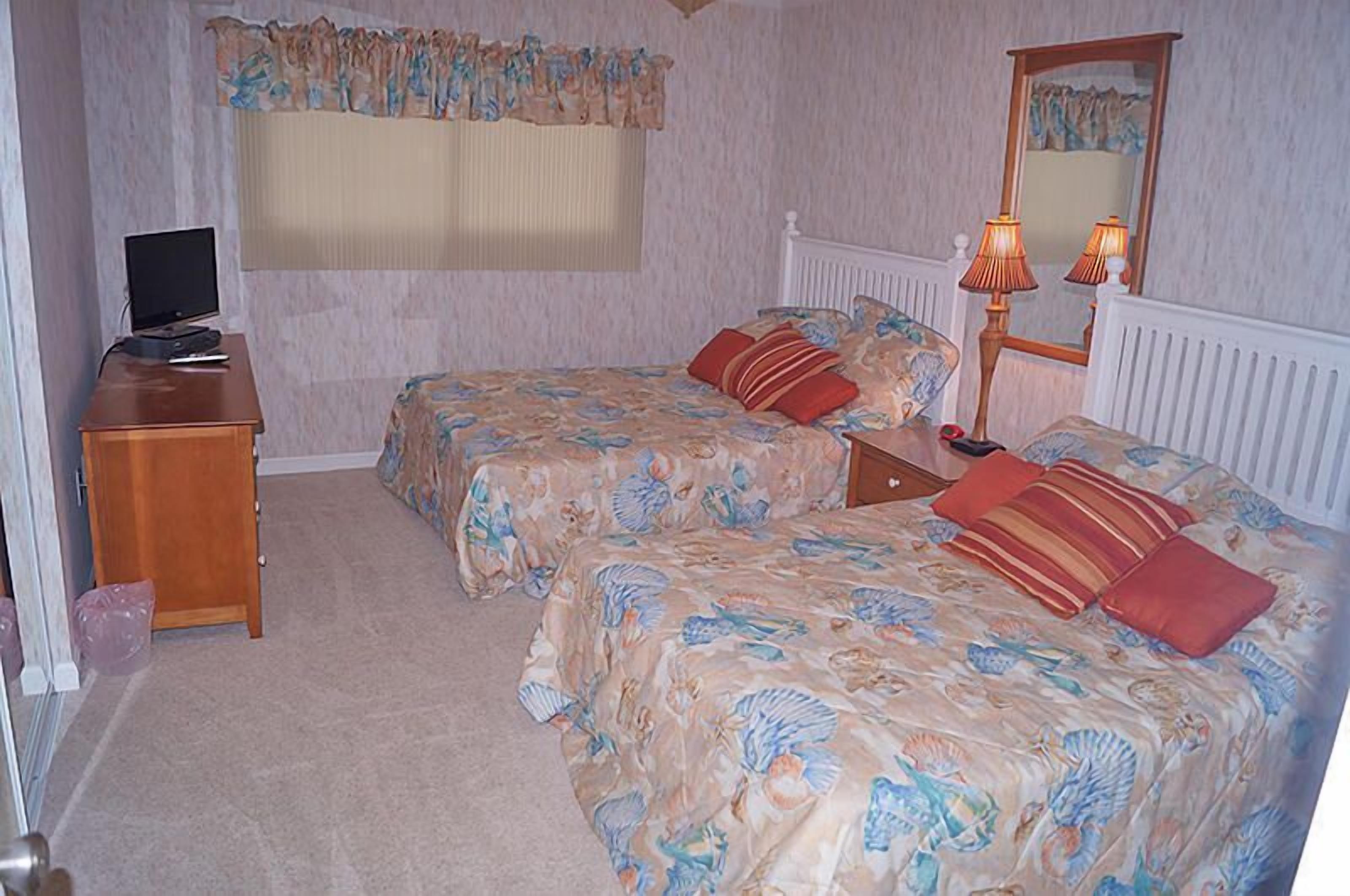Ein Schlafzimmer mit zwei Betten, einem Schreibtisch, einer Lampe und einem Spiegel.