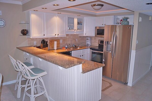 Una cocina moderna con armarios blancos, una isla central con taburetes de bar, electrodomésticos de acero inoxidable y un reloj en la pared.