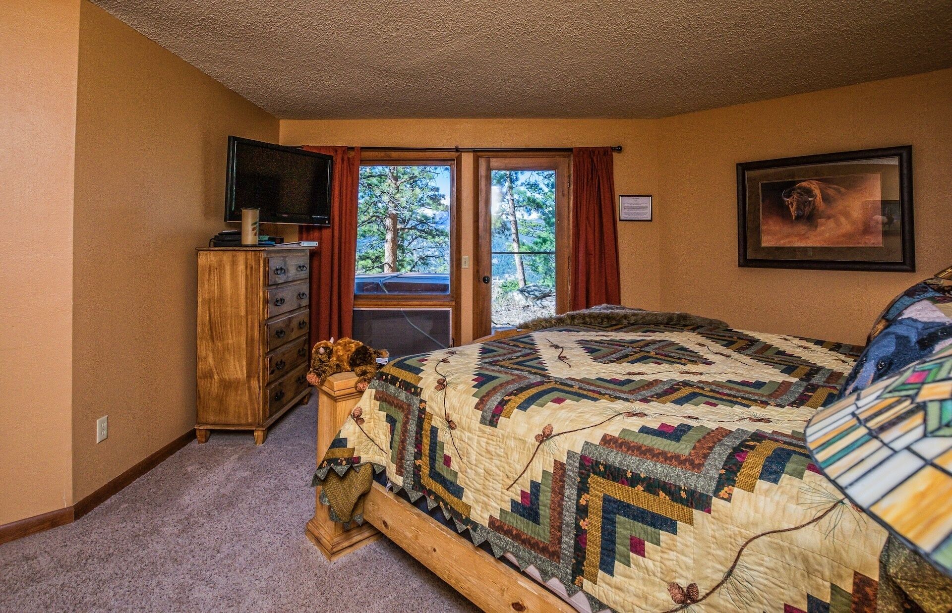 Une chambre à coucher avec un grand lit, une commode, un téléviseur et une fenêtre donnant sur les arbres.