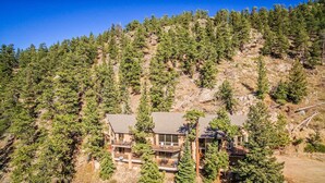 A two-story house with a balcony, surrounded by dense forest and rocky terrain. - Cedar Lower Luxury Vacation At Windcliff 2 Bedroom Home by RedAwning (Estes Park)