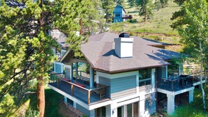 A modern two-story house with a large deck, surrounded by trees and a hilly landscape. - Adams Vacation At Windcliff 2 Bedroom Home by RedAwning (Estes Park)