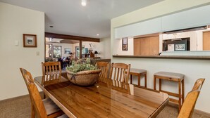 A dining area with a wooden table and chairs, a central plant, and a kitchen visible through an open door. - Adams Vacation At Windcliff 2 Bedroom Home by RedAwning (Estes Park)