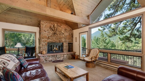 A cozy living room with a stone fireplace, leather sofas, and large windows offering a mountain view. - Adams Vacation At Windcliff 2 Bedroom Home by RedAwning (Estes Park)