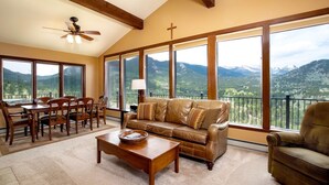 A spacious living room with a large sofa, a coffee table, and a dining area with chairs. There are large windows offering a mountain view. - Kintzle Family Vacation At Windcliff 4 Bedroom Home by RedAwning (Estes Park)