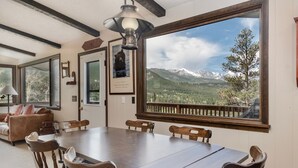 Comedor con una mesa grande y sillas, un ventilador de techo y vistas a montañas a través de un ventanal.