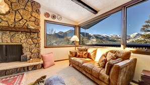 Una sala de estar acogedora con chimenea de piedra, sofá de cuero y ventanas amplias con vistas a las montañas.