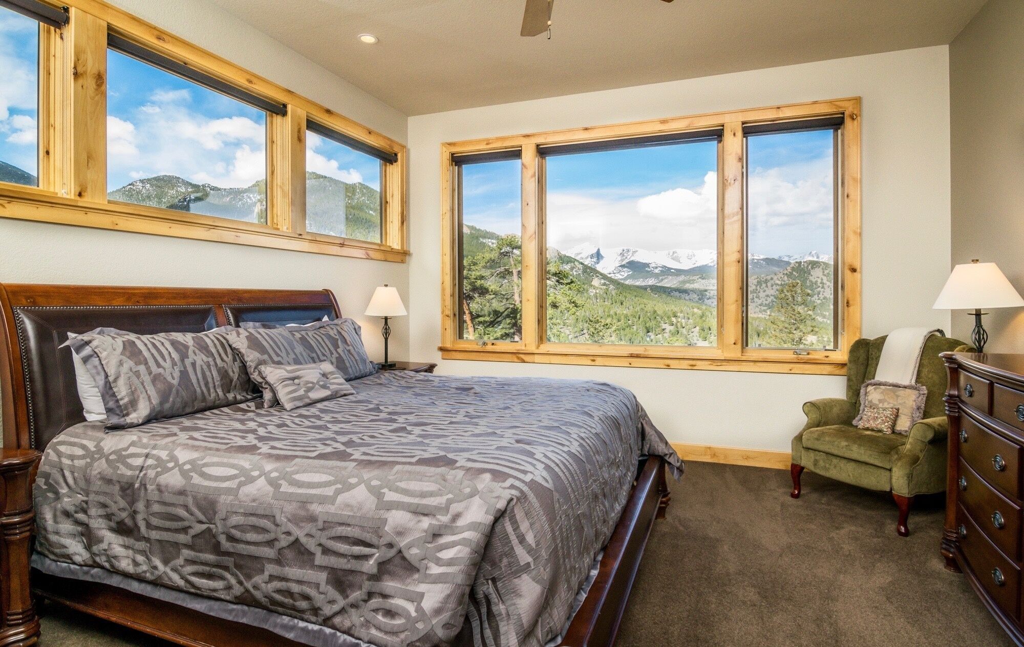 Un dormitorio con una cama grande, dos ventanas con vistas a las montañas, una silla y un aparador.