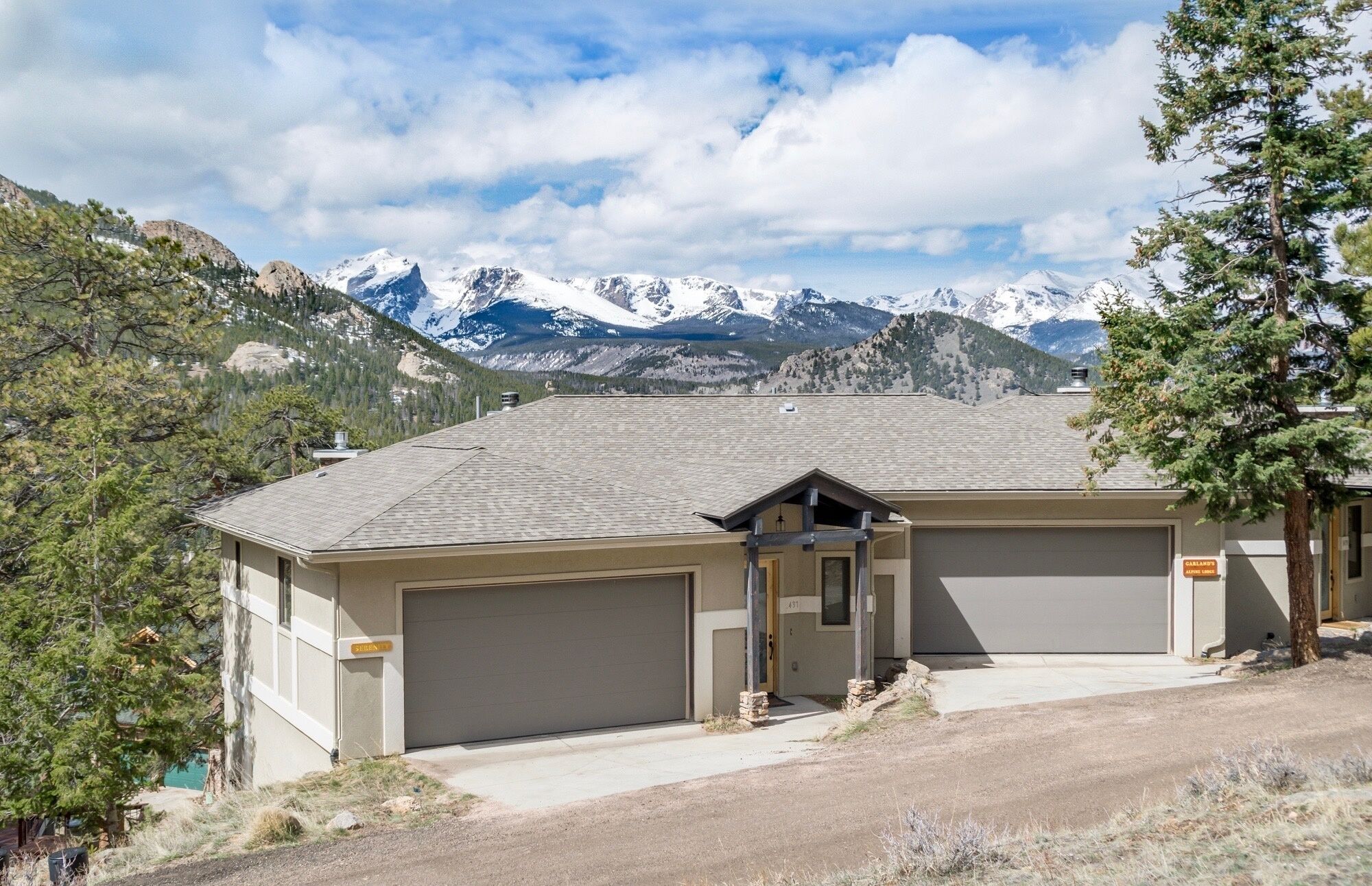 A two-story building with a garage and a covered driveway, surrounded by mountains and trees.