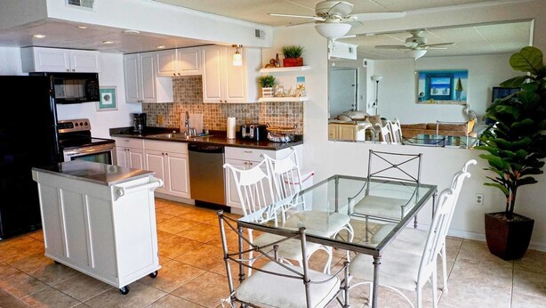 A modern kitchen with white cabinets, a central island, and a dining area with a glass table and white chairs. - Thunder Island 128c 2 Bedroom Condo by RedAwning (Ocean City)