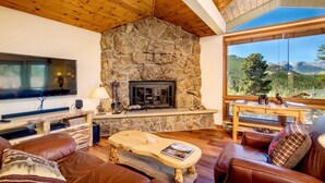 A cozy living room with a stone fireplace, leather sofas, a wooden coffee table, and a large TV.