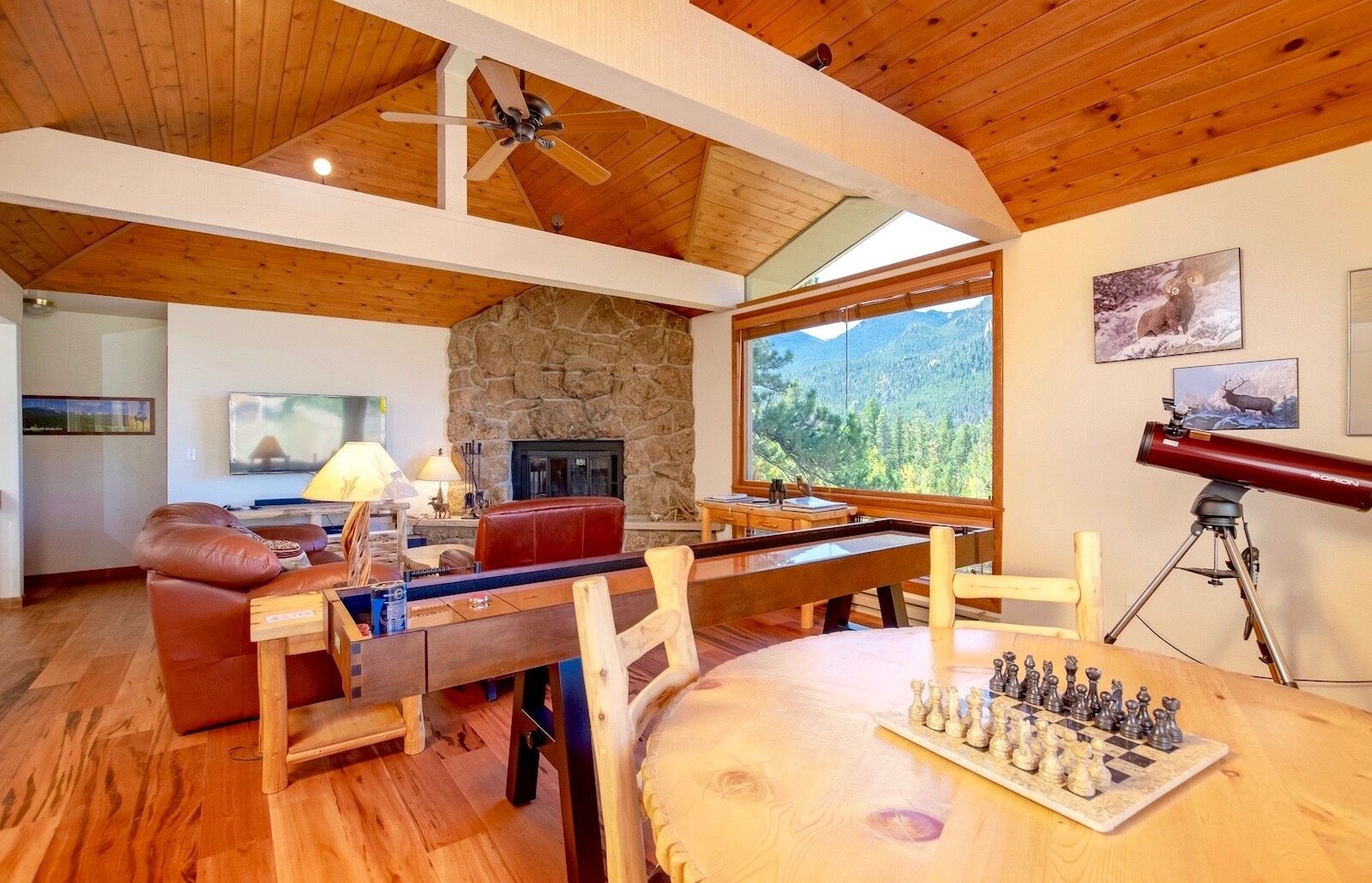 Ein gemütliches Wohnzimmer mit Kamin aus Stein, Holzboden und einem großen Fenster mit Blick auf die Berge.