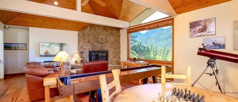 Ein gemütliches Wohnzimmer mit Kamin aus Stein, Holzboden und einem großen Fenster mit Blick auf die Berge.