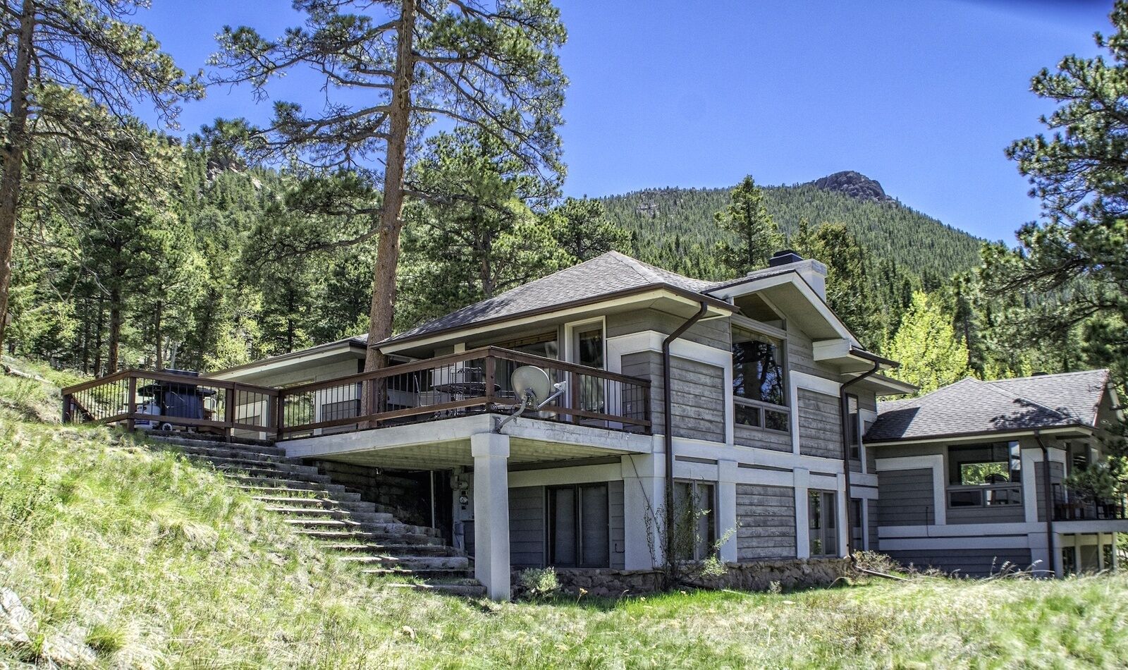 A two-story house with a balcony, surrounded by trees and a mountain in the background.