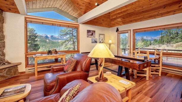 A cozy living room with leather furniture, a wooden table, and large windows offering mountain views.