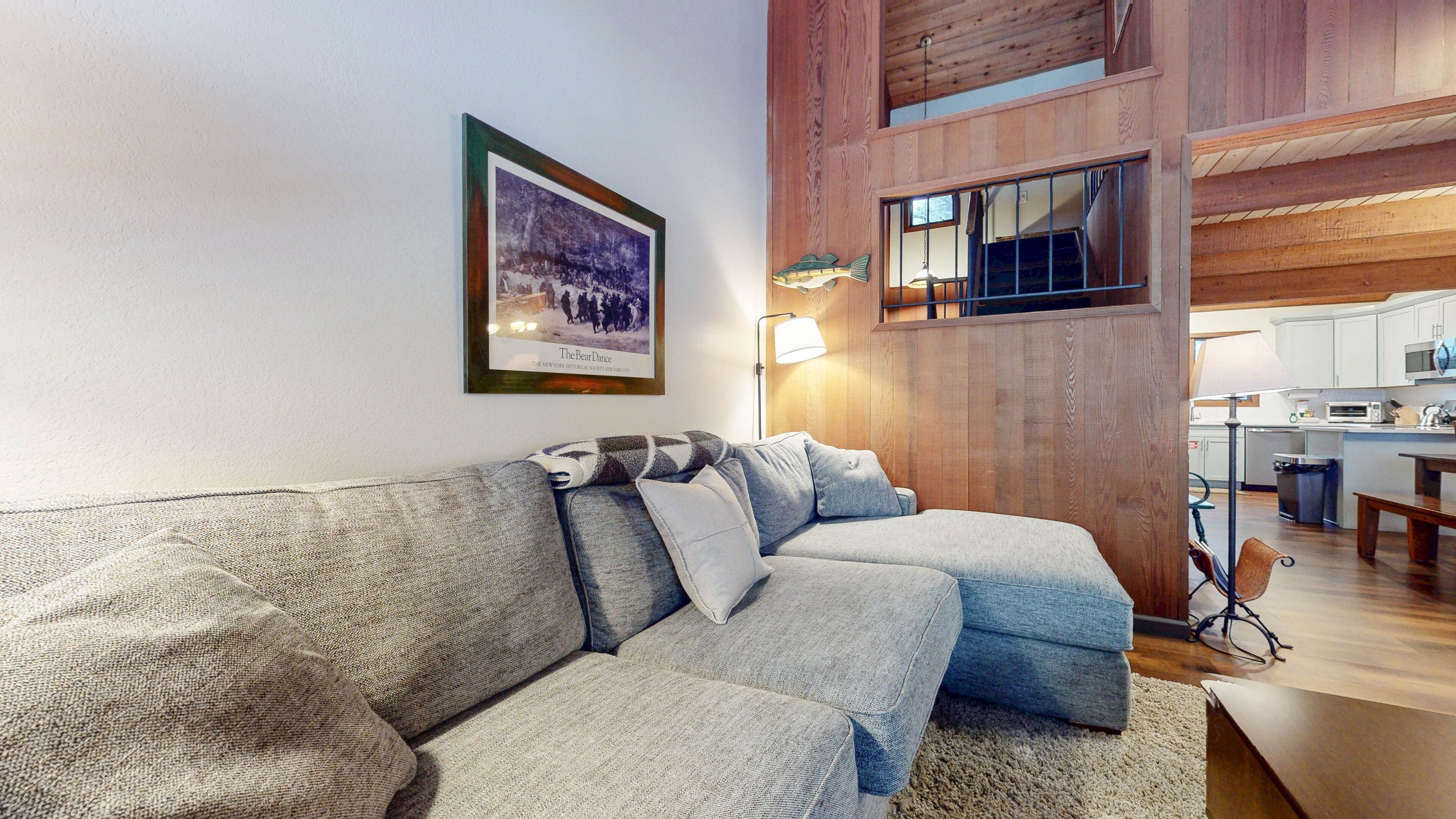 A cozy living room with a sectional sofa, a framed picture on the wall, and a wooden ceiling.