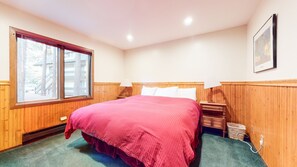 Une chambre avec un grand lit, un lambris en bois, une fenêtre, une table de chevet avec une lampe et un tableau accroché au mur.