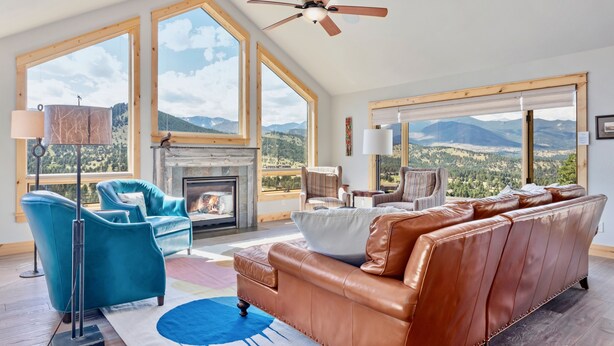 Amplia sala de estar con chimenea, ventanas grandes con vistas a la montaña y muebles modernos.