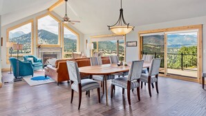 Amplia sala de estar con chimenea, una mesa de comedor con sillas y ventanas grandes con vistas a las montañas.