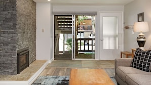 A living room with a stone fireplace, a sofa, a coffee table, and a sliding glass door leading to an outdoor balcony. - Timber Ridge Unit 2e 1 Bedroom Condo by RedAwning (Aspen)