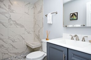 Een badkamer met marmeren tegels, een wit toilet, een wastafel met twee kraan en een handdoekrek met twee handdoeken.