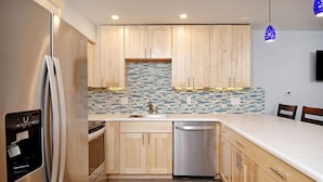 A modern kitchen with wooden cabinets, a stainless steel refrigerator, dishwasher, and a tiled backsplash. - Timber Ridge Unit 2e 1 Bedroom Condo by RedAwning (Aspen)