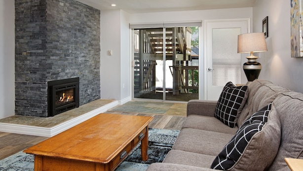 A living room with a stone fireplace, a sofa with patterned cushions, and a wooden coffee table. - Timber Ridge Unit 2e 1 Bedroom Condo by RedAwning (Aspen)