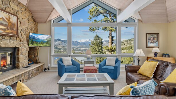 A cozy living room with a stone fireplace, large windows offering mountain views, and comfortable seating. - Werlein Family Vacation At Windcliff 4 Bedroom Home by RedAwning (Estes Park)