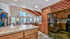A spacious kitchen with wooden cabinets, a large refrigerator, and a stone fireplace. - Your Roomy Northstar Retreat Awaits by RedAwning (Truckee)