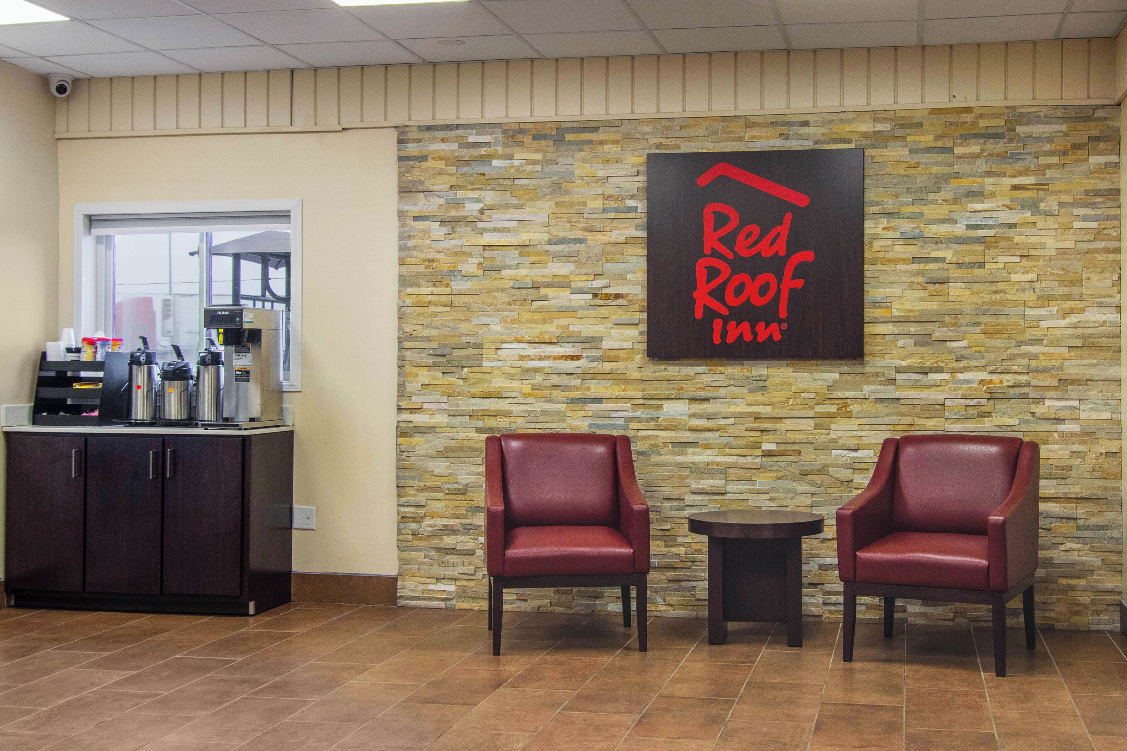 A Red Roof Inn reception area with a stone wall backdrop, a coffee machine, and two leather chairs.