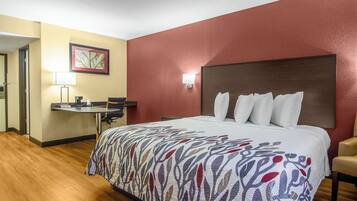 Una habitación de hotel con cama, escritorio, silla, lámpara y un cuadro en la pared.
