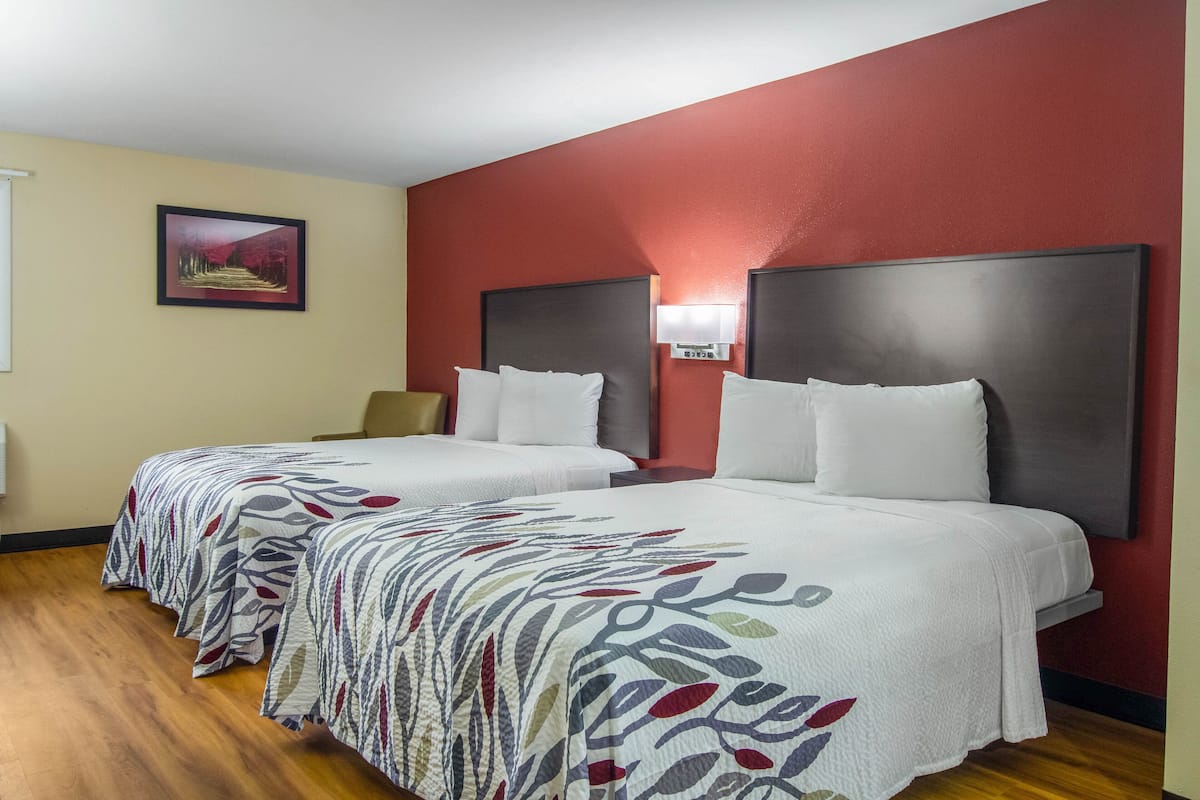A hotel room with two beds, a red accent wall, and a framed picture on the wall.
