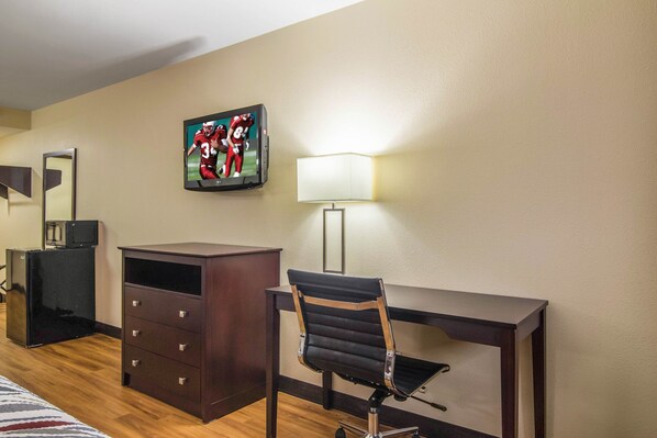 A hotel room with a desk, chair, dresser, TV, and lamp. - Red Roof Inn Perrysburg (Perrysburg)