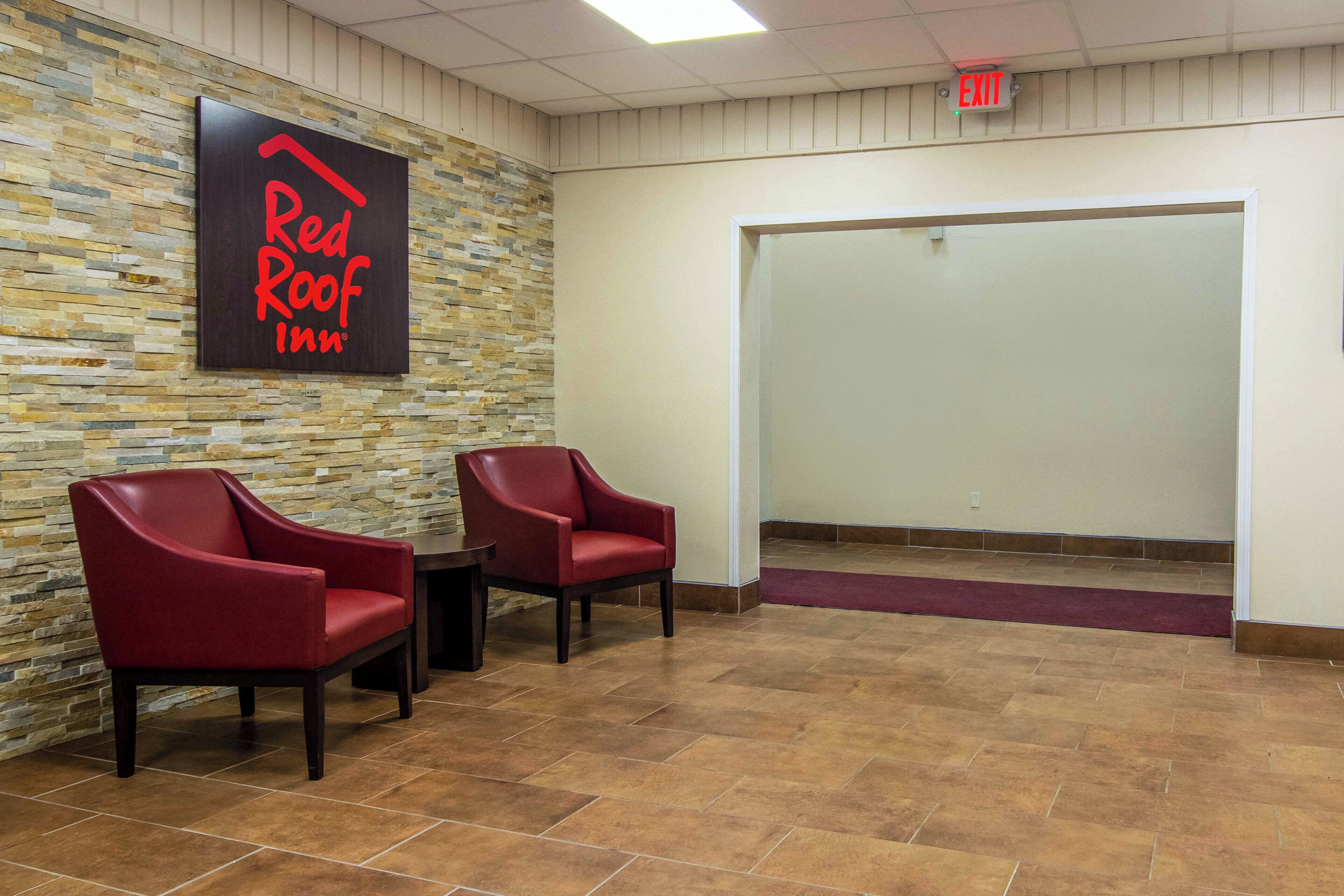 Vestíbulo de Red Roof Inn con dos sillas rojas, una pared de piedra y una señal de salida.