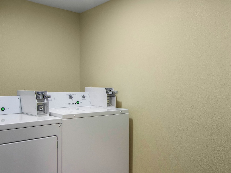 Uma área de lavanderia com duas máquinas de lavar e uma secadora, um painel de controle e uma balança fixada na parede.