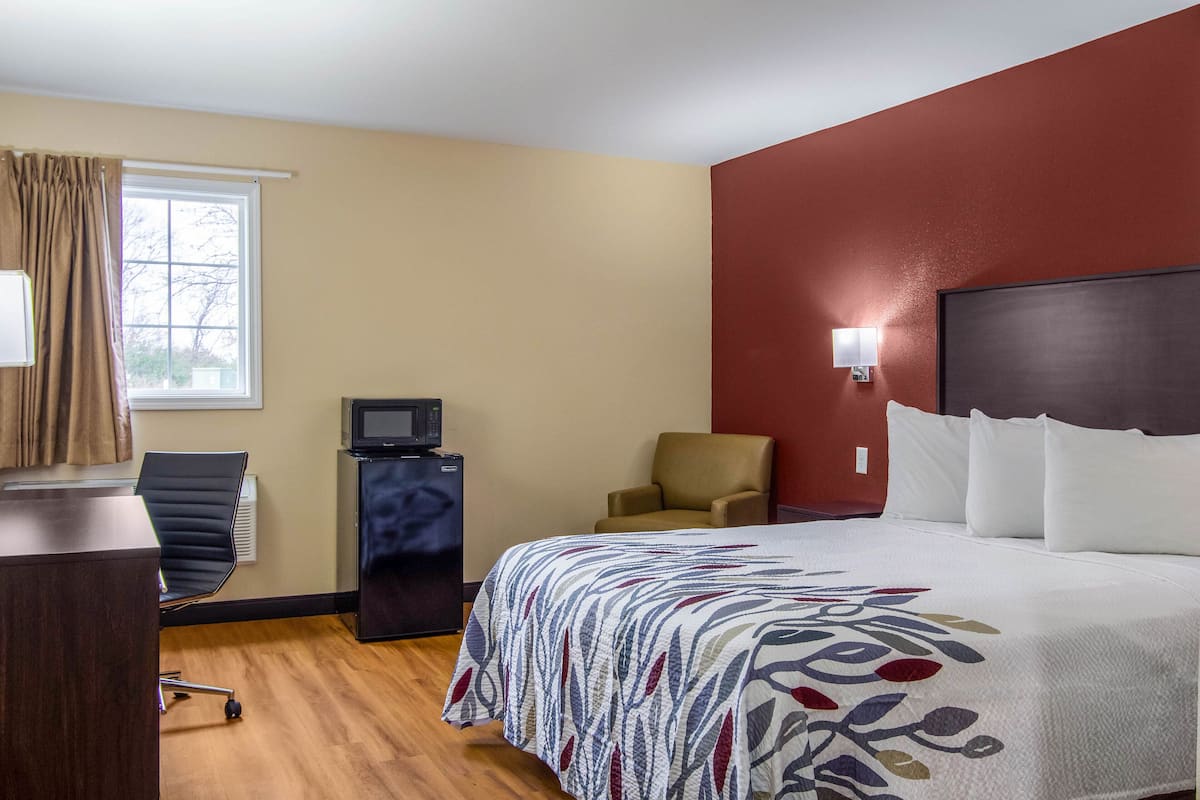A hotel room with a bed, a desk, a chair, a TV, and a window with curtains.